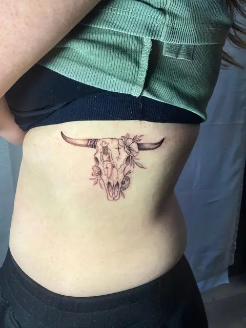 A bull skull with a small figure, a cross, and flowers, on the side.
