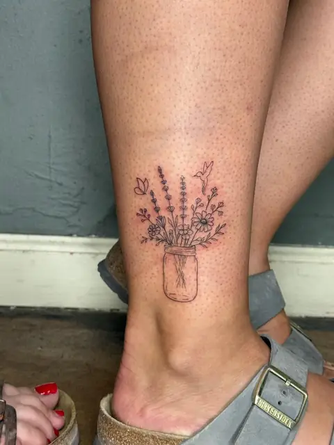 A jar of lavender and daisies, with a hummingbird and a butterfly, on the ankle.
