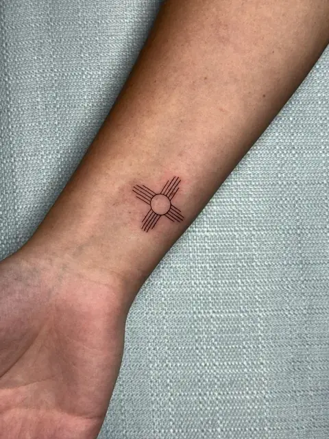 The Zia sun, New Mexico’s symbol, in a clean line on the wrist.